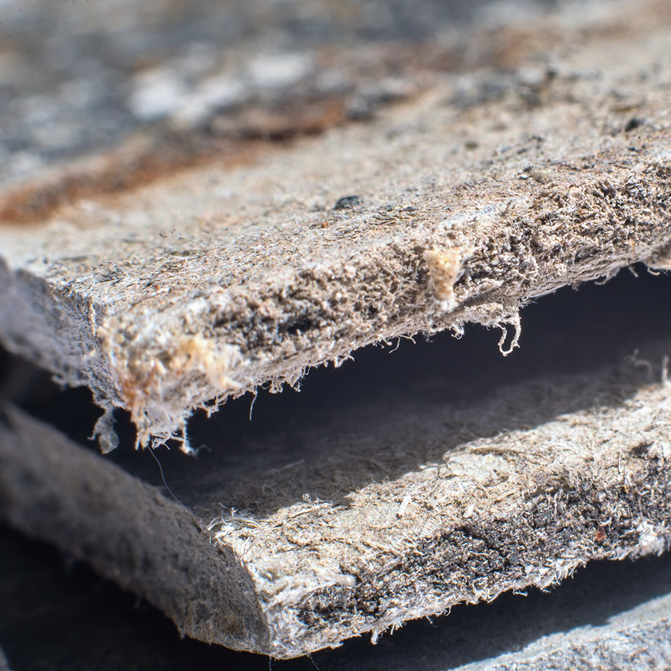 Nahaufnahme einer alten faserigen Faserzementplatte mit sichtbar ausgefransten Bruchkanten