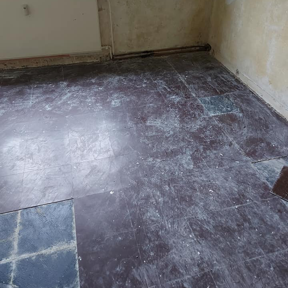 Alter dunkler Bodenbelag mit teilweise entfernten Platten und freigelegtem Untergrund in einem Bestandsraum