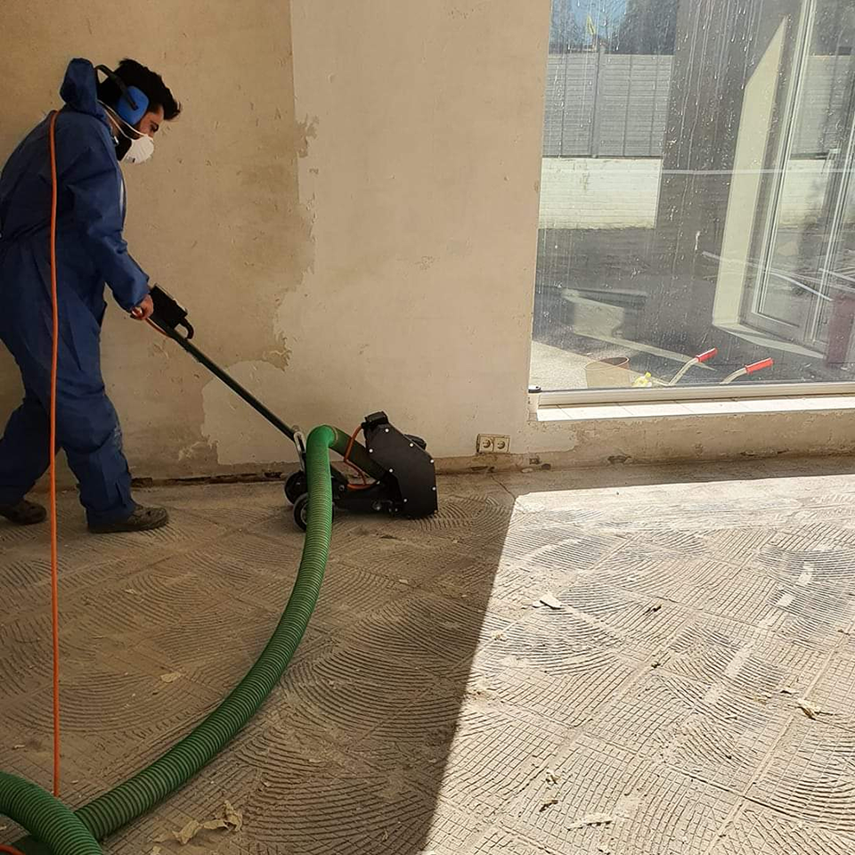 Fachkraft mit Atemschutz bei der maschinellen Entfernung von Kleberresten auf einem Boden mit angeschlossener Absaugung